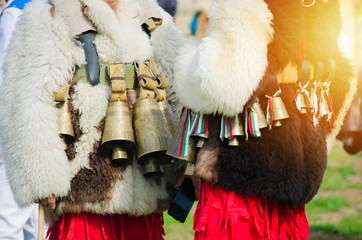 Costumed Bulgarian men Kuker who perform traditional rituals. White furry jackets with bells and ribbons with colors of Bulgaria. Warm sunlight effect. Ethnic celebration
