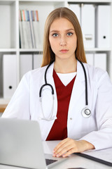 Brunette female doctor using laptop computer in hospital. Healthcare, insurance and medicine concept
