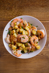 Shrimps with scallions and crispy potatoes in white bowl on wooden background. overhead, vertical