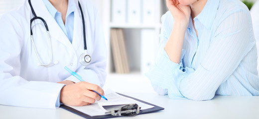 Unknown female doctor and patient discussing something while sitting at the table at hospital....
