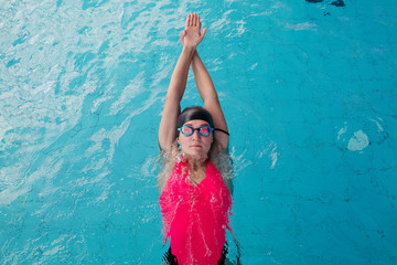 View from above of young sporty girl in goggles and cap swimming in the blue water pool. Woman...
