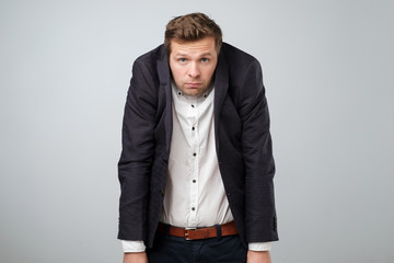 Caucasian young man in too big suit. He is offended and looking stressed.
