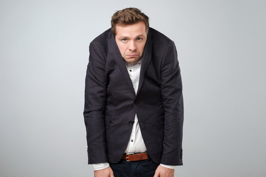 Caucasian young man in too big suit. He is offended and looking stressed.