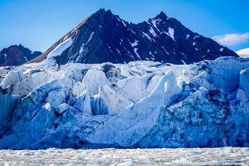 Dramatic mountains rise out from behind the jagged surface of a glacier in Svalbard in the Norwegian high arctic