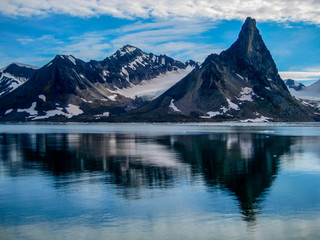 Dramatic mountains reflect in the calm, icy waters of Svalbard in the Norwegian high arctic