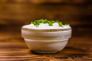 Glass bowl with sour cream and chopped green onion on wooden table