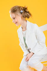 A teenage girl in white clothes is sitting on a chair on a yellow background.