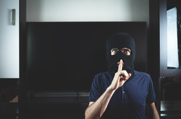 Thief with black balaclava making silence gesture.