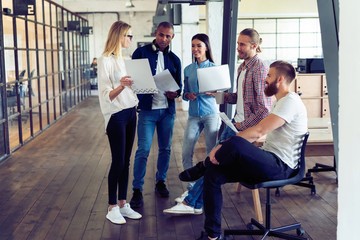 Working as a team. Full length of young modern people in smart casual wear planning business strategy while young woman pointing at large paper in the office hallway.