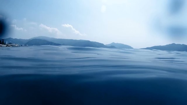 Slow motion video of camera slowly submerging into the deep sea at bright sunny day