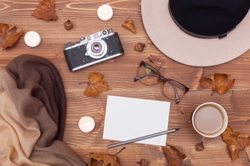 Autumn composition. Flat lay, top view. Woman's hat, scarf, glasses, diary, bouquet of flowers, retro camera, candles, cup of coffee and yellow leaves on a wooden background with space for text