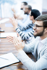 Side view of smiling businessman clapping hands together with his colleagues at business seminar