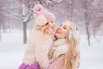 mother with long blond curls hugs her beautiful little daughter in a pink hat with a bubo