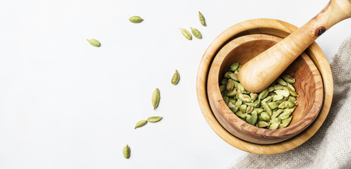 Dried cardamom in wooden bowl with pestle, white background, top view