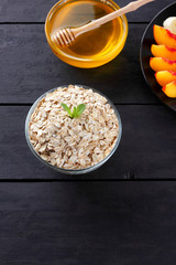 Oatmeal, honey and sliced fruit with mint for breakfast. Oat flakes, banana slices, sliced apple and peaches. Oatmeal, various fruits and honey on black wooden boards. Healthy food
