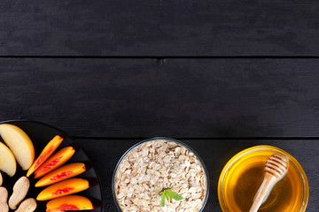 Oatmeal, honey and sliced fruit with mint for breakfast. Oat flakes, banana slices, sliced apple and peaches. Oatmeal, various fruits and honey on black wooden boards. Healthy food