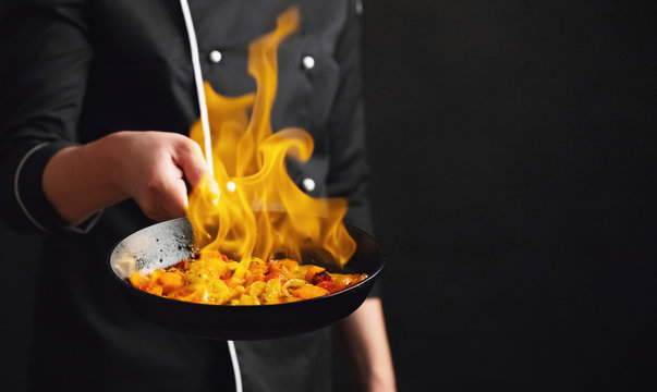 Professional chef and fire. Cooking vegetables and food over an open fire on a dark background. Hotel service photo background. With copy space for your text. Flambeau
