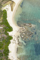 Aerial view of an amazing rocky and green coast with small beaches bathed by a transparent and turquoise sea. Sardinia, Italy.