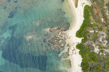 Aerial view of an amazing rocky and green coast with small beaches bathed by a transparent and turquoise sea. Sardinia, Italy.