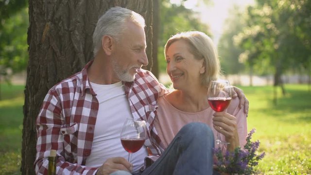 Happy mature woman and man drinking wine and enjoying romantic date in park