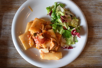 Pasta with meat tomato sauce and salad of green vegetables on a white plate