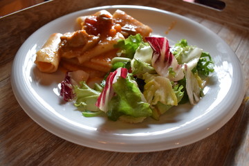 Pasta with meat tomato sauce and salad of green vegetables on a white plate