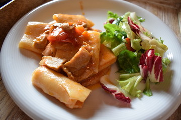 Pasta with meat tomato sauce and salad of green vegetables on a white plate