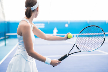 Back view portrait of female tennis player serving ball and holding racket in indoor court, copy space © Seventyfour