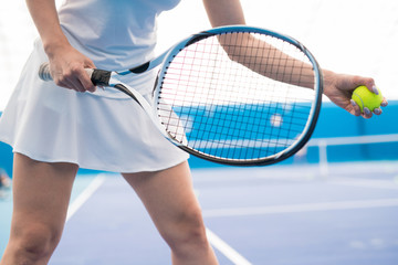 Mid-section closeup of unrecognizable young woman holding racket while playing tennis in indoor court, copy space
