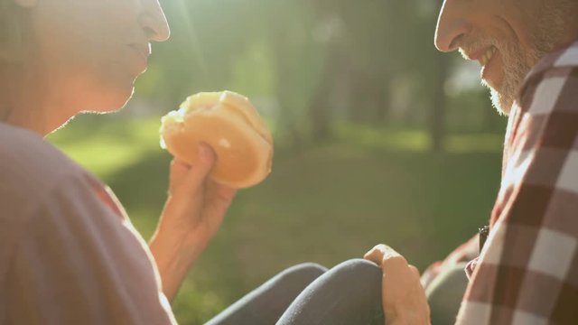Female and male pensioners eating burger on picnic, romantic date, close-up