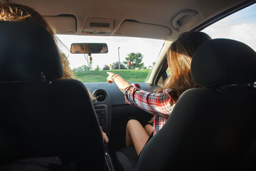 Young women sitting in the front seats of the car pointing where to go on a vacation trip. 