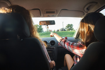Young women sitting in the front seats of the car pointing where to go on a vacation trip. 