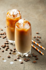 Ice coffee in a tall glass with cream poured over and coffee beans. Cold summer drink on a brown...