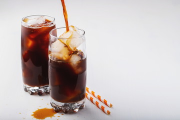 Ice coffee in a tall glass with cream poured over and coffee beans. Cold summer drink on white background with copy space