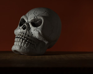 Halloween background concept. Front view of human skull, gloomy light on wooden table and orange...