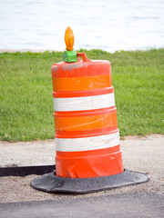 Photograph of a single orange construction barrel near an asphalt bike path on the lakefront in Chicago with grass and water beyond.