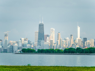 Gorgeous view of the Chicago skyline including new and old skyscrapers across the water of Lake Michigan with grass in the foreground of the near shore.