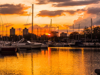 Gorgeous sunset with vivid colorful orange and yellow colored clouds in the sky above and boats reflecting in the water at Montrose Harbor in Chicago.