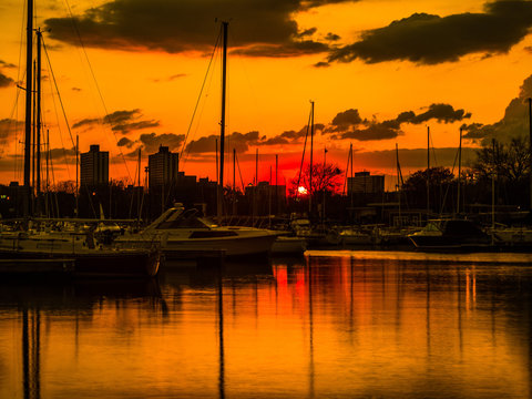 Gorgeous sunset with vivid colorful orange and yellow colored clouds in the sky above and boats reflecting in the water at Montrose Harbor in Chicago.