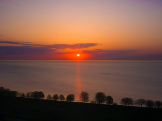 Beautiful sunrise over Lake Michigan in Chicago with calm water and orange and yellow colors reflecting from the sun and clouds above.