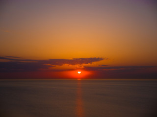 Beautiful sunrise photograph with vibrant orange and yellow colors over the dark waters of Lake Michigan in Chicago with layers of clouds in the sky above.