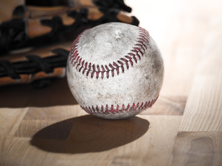 Close up sports background image of an old used weathered leather baseball laying in front of a ball glove on a wood butcher block counter showing intricate detailing and red laces.