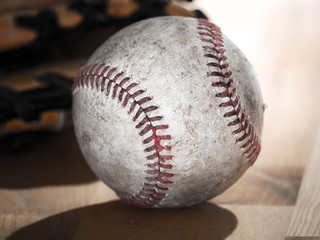 Close up sports background image of an old used weathered leather baseball laying in front of a ball glove on a wood butcher block counter showing intricate detailing and red laces.