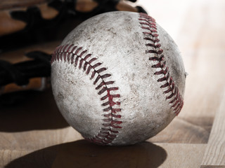 Close up sports background image of an old used weathered leather baseball laying in front of a ball glove on a wood butcher block counter showing intricate detailing and red laces.
