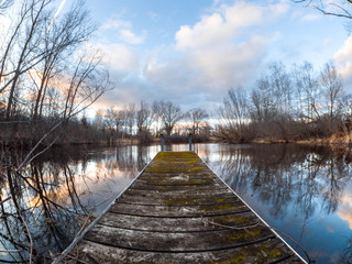 Beautiful landscape photograph of a weathered wood and steel pier sticking out into a pond in Wisconsin at sunset with the water reflecting the colorful clouds and trees making a fantastic background.