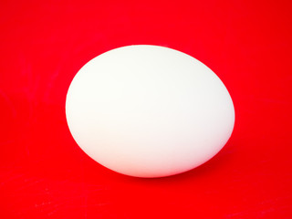 Close-up photograph of a real large plain white chicken egg on vibrant red solid color cutting board background making a beautiful eye catching background for the easter holiday.