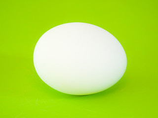 Close-up photograph of a real large white chicken egg on vibrant green solid color cutting board background making a beautiful eye catching background for the easter holiday.