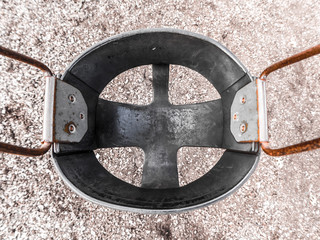 Close up photograph of a black rubber child's swing with weathered and rusted metal hooks and chains and brown dirt and wood chips below.