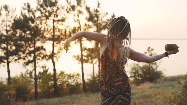 Hippie attractive woman dances and conjures with a human skull. Woman in the image of a witch at sunset or sunrise