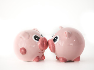 Close up photograph of two pink round pig ceramic salt and pepper shakers kissing or touching snouts facing each other isolated on a white background with space around the animal shaped objects.